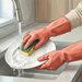 Persona con guantes de goma rosas lavando un plato blanco con una esponja bajo el grifo de la cocina para proteger las manos del agua y los detergentes.