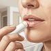 Primer plano de una mujer aplicándose bálsamo labial en los labios visiblemente secos y agrietados.