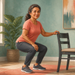 Mujer adulta realizando una sentadilla con apoyo en una silla dentro de casa, con una mano sobre el respaldo y las rodillas flexionadas.