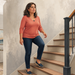 Mujer adulta subiendo una escalera en casa, con una pierna elevada sobre el siguiente peldaño y gesto atento durante el movimiento.