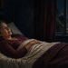 Mujer despierta acostada en la cama durante la noche, con tráfico de coches visible a través de la ventana y luces de la calle en el exterior.