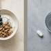 Cuenco con yogur, arándanos y granola junto a un vaso de agua y un comprimido blanco en una composición dividida en dos partes.
