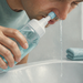 Hombre adulto realizando un lavado nasal sobre un lavabo con una botella de irrigación, mientras el líquido sale por la otra fosa nasal.