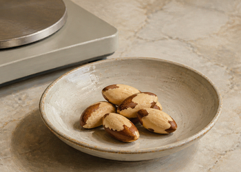 Cuenco con varias nueces de Brasil sobre una encimera clara, junto a una balanza de cocina.