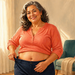 Mujer adulta sonriente mostrando la zona del abdomen mientras sujeta la cintura de un pantalón azul oscuro, de pie en una sala luminosa.