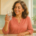 Mujer madura sonriente sostiene un vaso de agua con burbujas en una cocina luminosa, junto a una botella transparente y un grifo.