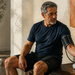 Hombre adulto sentado después de hacer ejercicio mientras se mide la presión arterial con un tensiómetro automático, junto a unas mancuernas.
