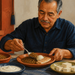 Hombre adulto mayor come un plato con lentejas, huevo y pescado, acompañado de yogur y queso sobre la mesa.