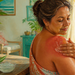 Mujer adulta aplicándose gel sobre un hombro enrojecido por una quemadura solar leve, junto a una hoja de aloe vera y un cuenco con gel.