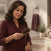 Mujer adulta en un baño observando un cepillo de pelo con varios cabellos atrapados entre las cerdas, junto a un lavabo y un espejo.
