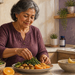 Mujer adulta mayor prepara un plato con verduras de hoja verde, naranja y otros alimentos, con un plátano visible en un recipiente sobre la encimera.