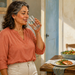 Mujer adulta bebiendo un vaso de agua en una cocina, junto a una mesa servida con salmón, ensalada y una jarra de agua.