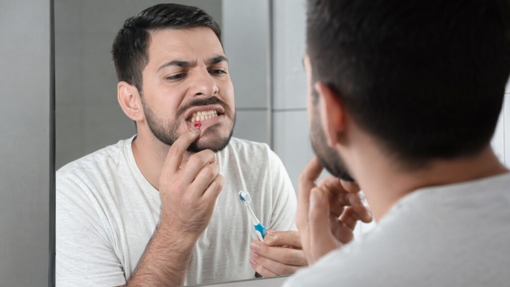 Pessoa observa a gengiva sangrando durante a escovação em uma cena de cuidado precoce.